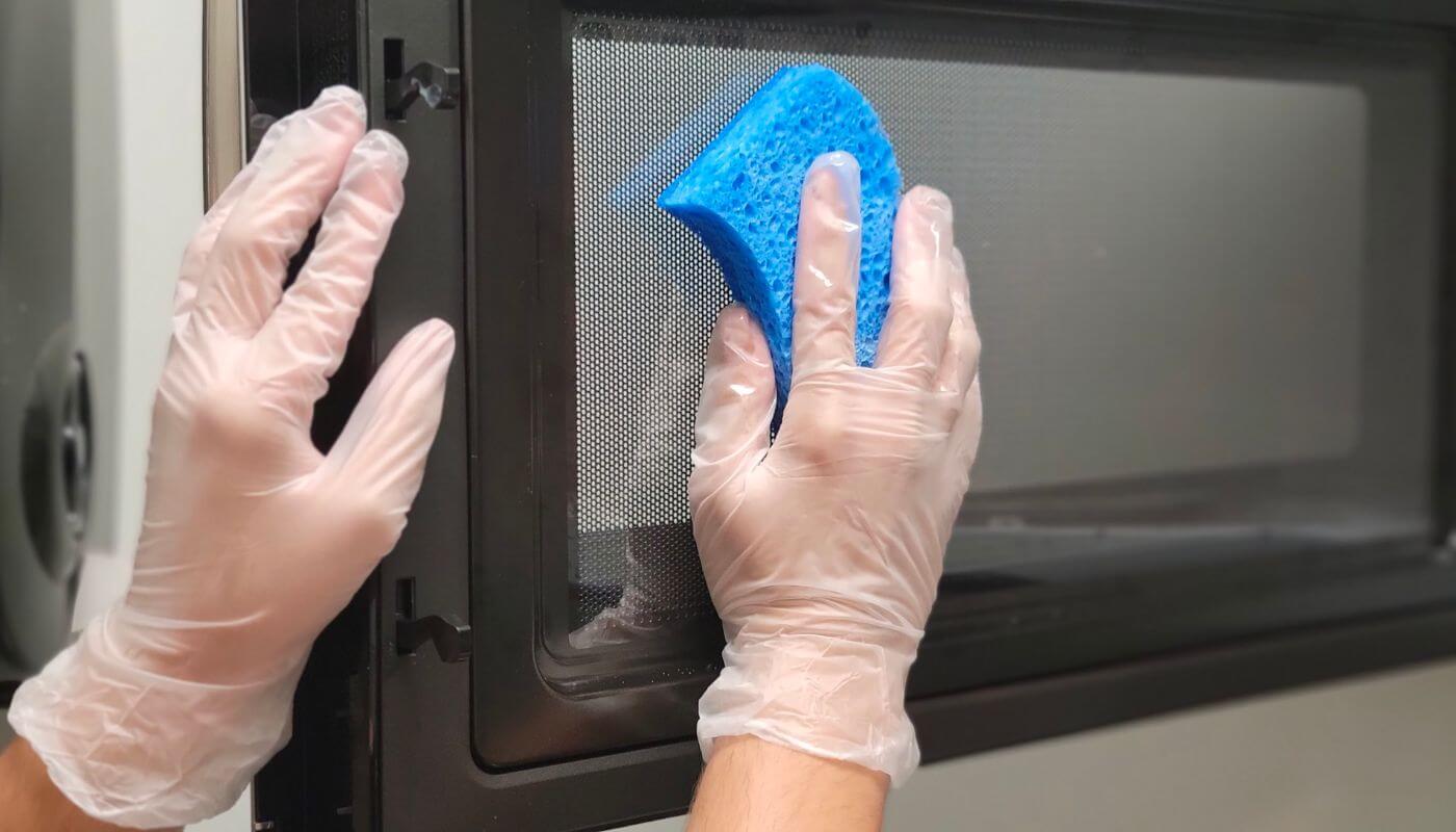 cleaning a microwave wearing clear latex gloves